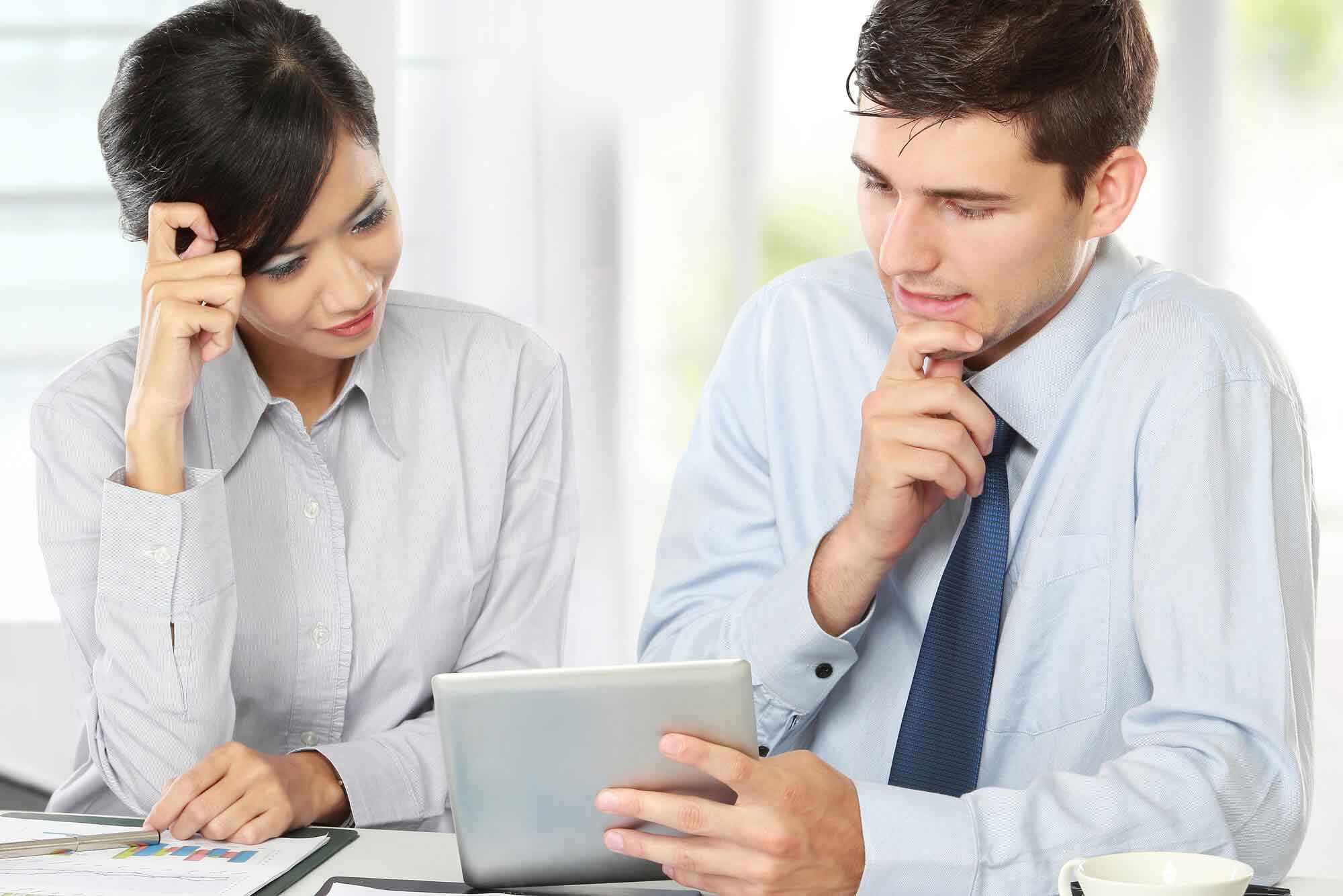 Image of two young business partners using touchpad at meeting